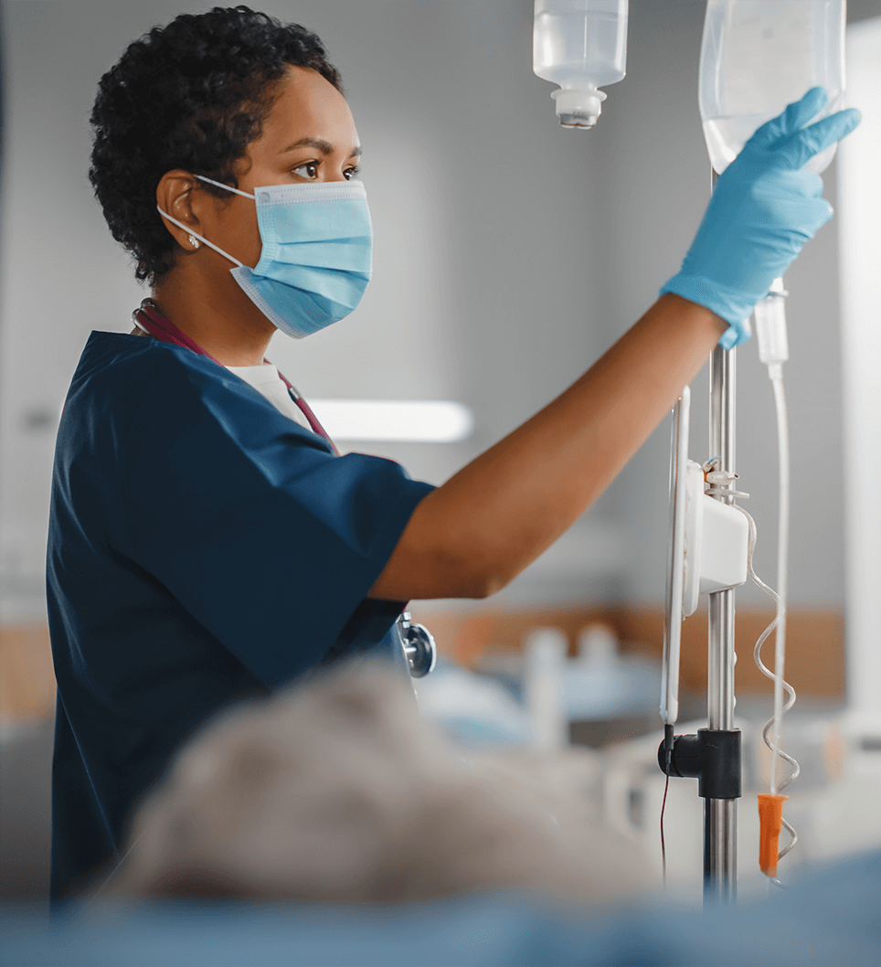 A nurse in a mask adjusting an IV drip at a patient's bedside